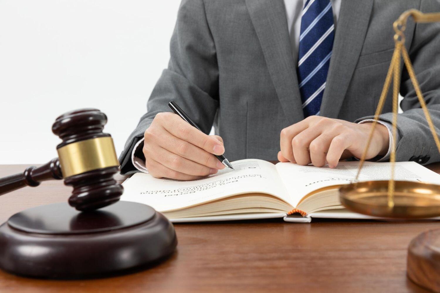 A legal professional writes in a notebook, with a gavel and scales of justice on the desk, symbolizing the practice of law.